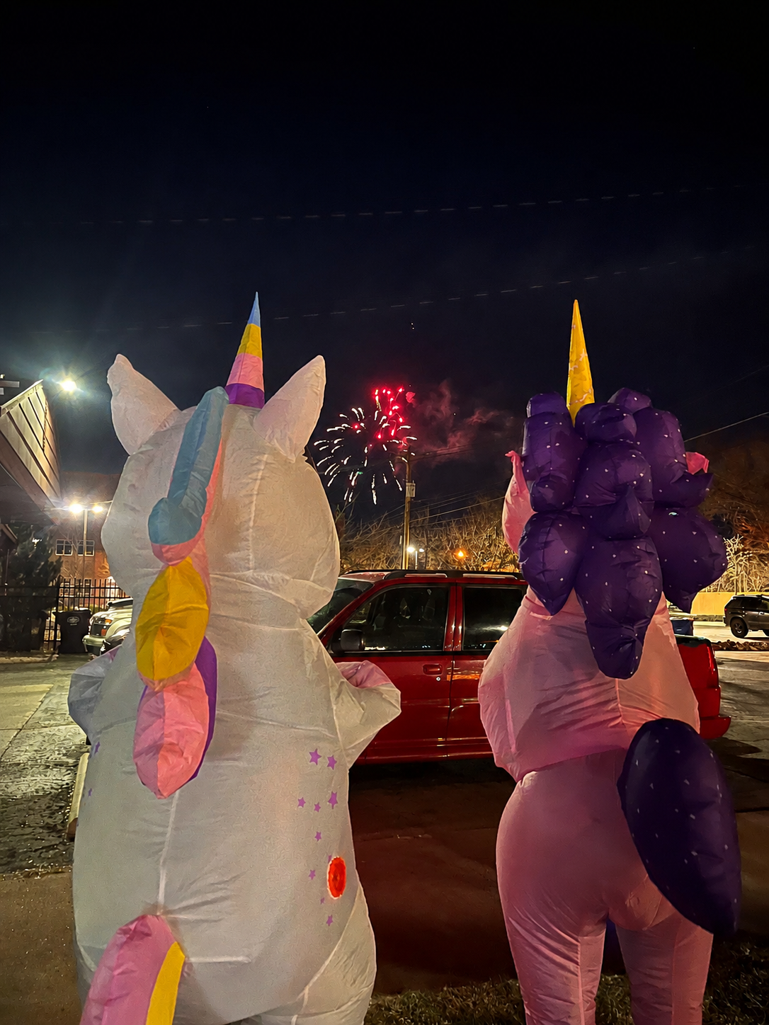 Two people wearing inflatable unicorn costumes at a nighttime parade